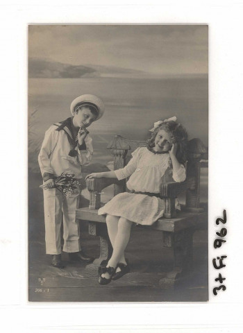 Petit marin offrant du muguet à une fillette assise sur un bac devant la mer.