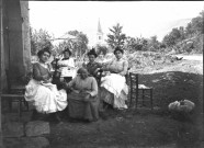 Groupe de cinq femmes assises devant une maison en pierre.