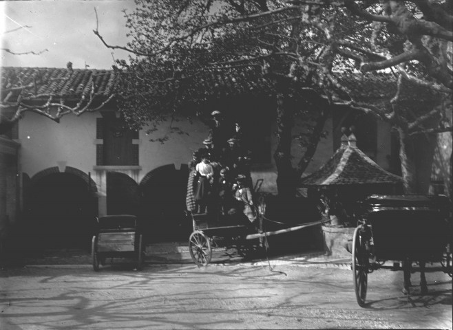 Groupe d'hommes et de femme sur un charriot sans attelage, au milieu de la [cour d'une ferme].