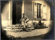 Jeune homme sur un vélo devant le perron d'une maison bourgeoise.