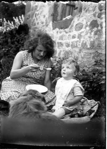 Herminie donnant à manger à Olivier sur une couverture dans le jardin d'une maison en pierre [été 1931].