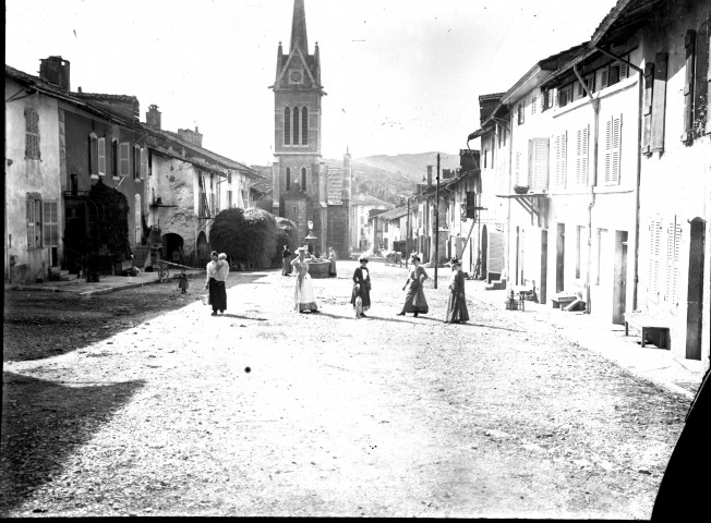 Rue d'un village avec église et promeneuses.