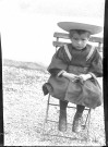 Garçonnet en costume marin avec chapeau assis sur une chaise de jardin.